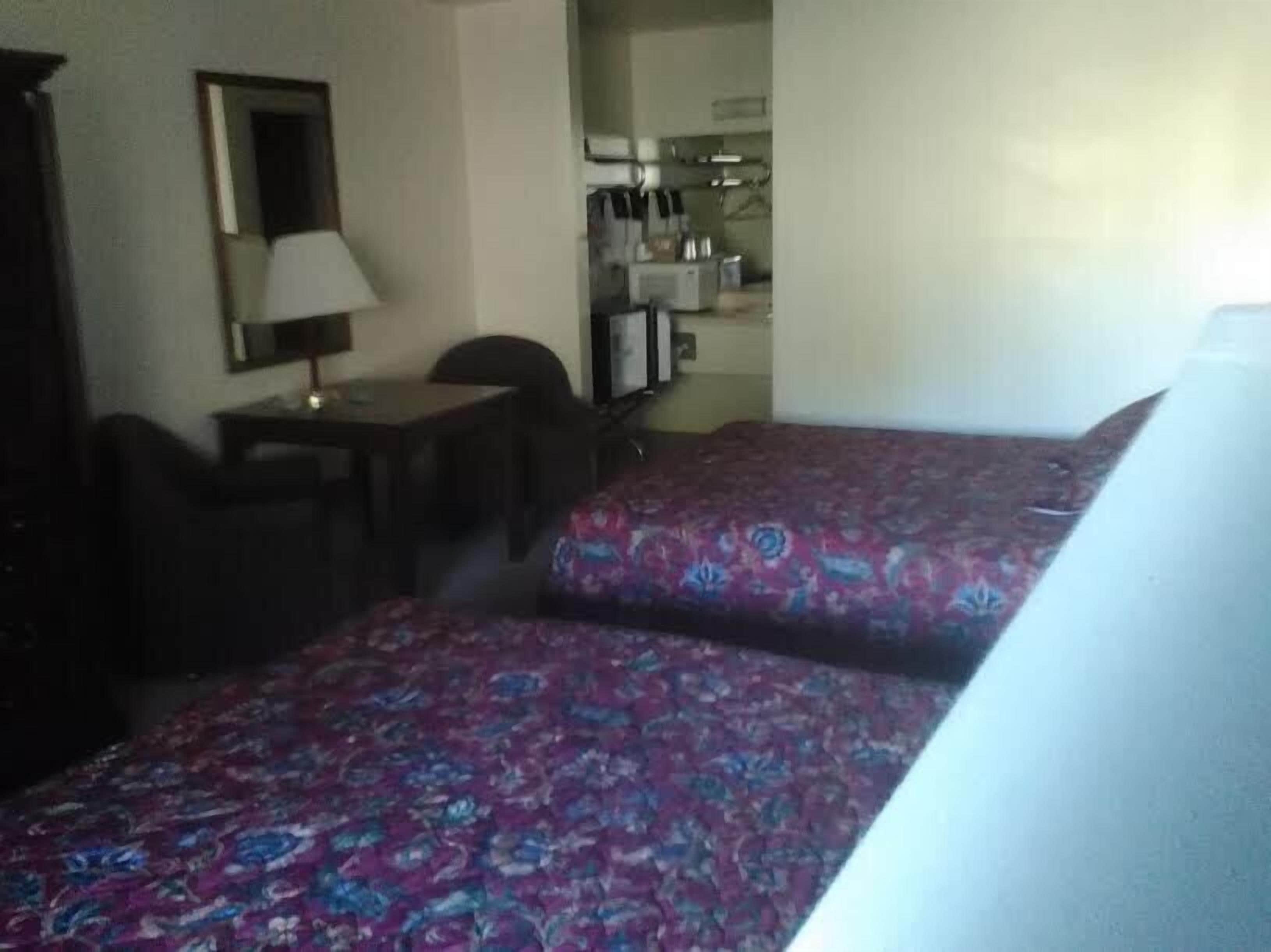 Ein Hotelzimmer mit zwei Betten, einem Schreibtisch, einem Stuhl und einer kleinen Küchenzeile.