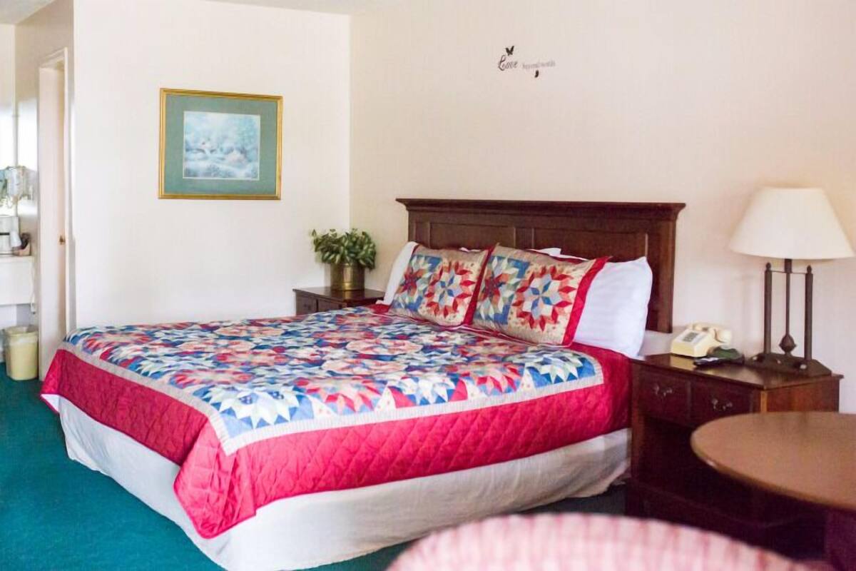 A neatly made bed with a colorful quilt, a bedside table with a lamp, and a framed picture on the wall.