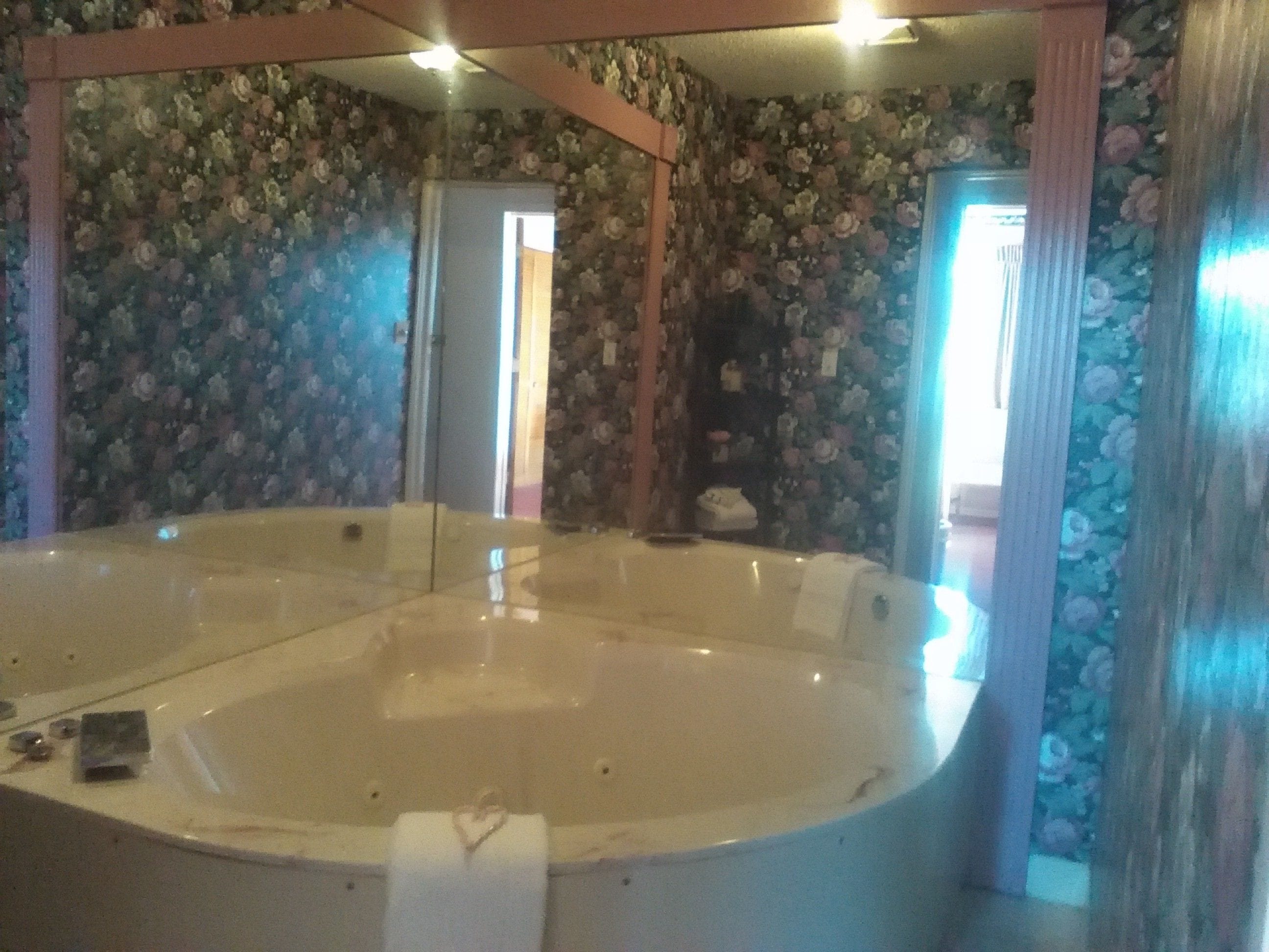 Una habitación con una bañera grande, papel tapiz floral y una estructura de techo de madera.