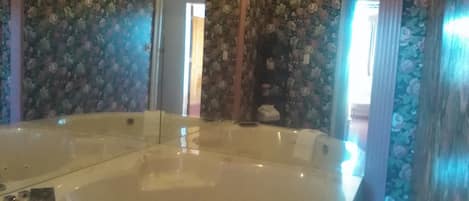 Una habitación con una bañera grande, papel tapiz floral y una estructura de techo de madera.