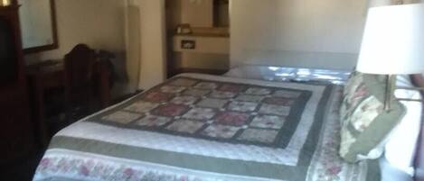 Un dormitorio con cama, mesita de noche, lámpara y un adorno en la pared.