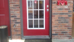 Una puerta roja con una ventana, un muro de ladrillo y un cartel que dice 'Happy Valentine's'.