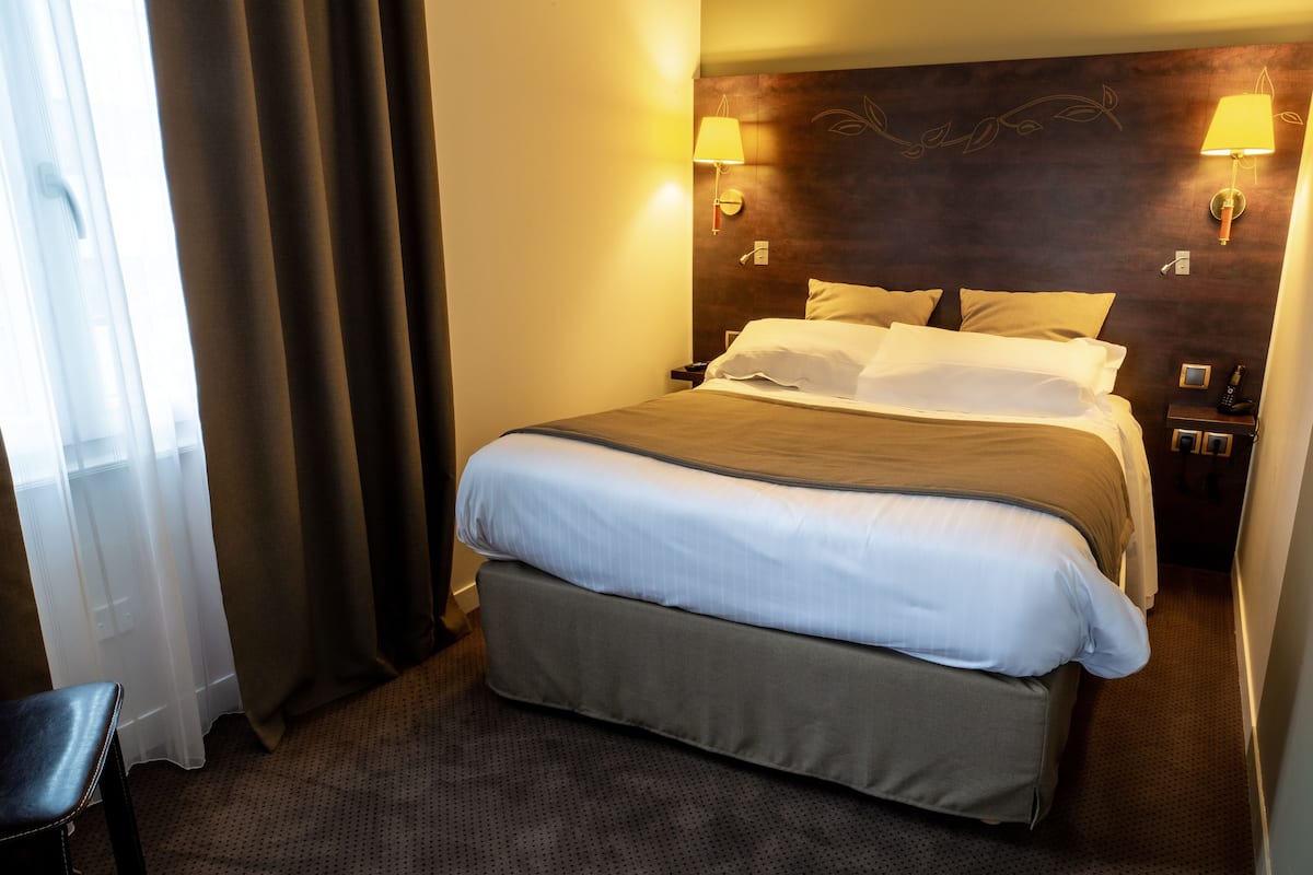 A hotel room with a large bed, two bedside lamps, a wooden headboard, and a chair.