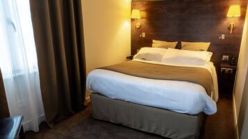 Una habitació d'hotel amb un llit gran, dues làmpades laterals, un panell de capçal de fusta i una cadira.
