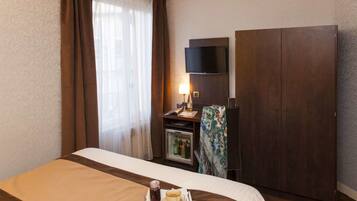 Habitación de hotel con cama, minibar, televisión y armario.