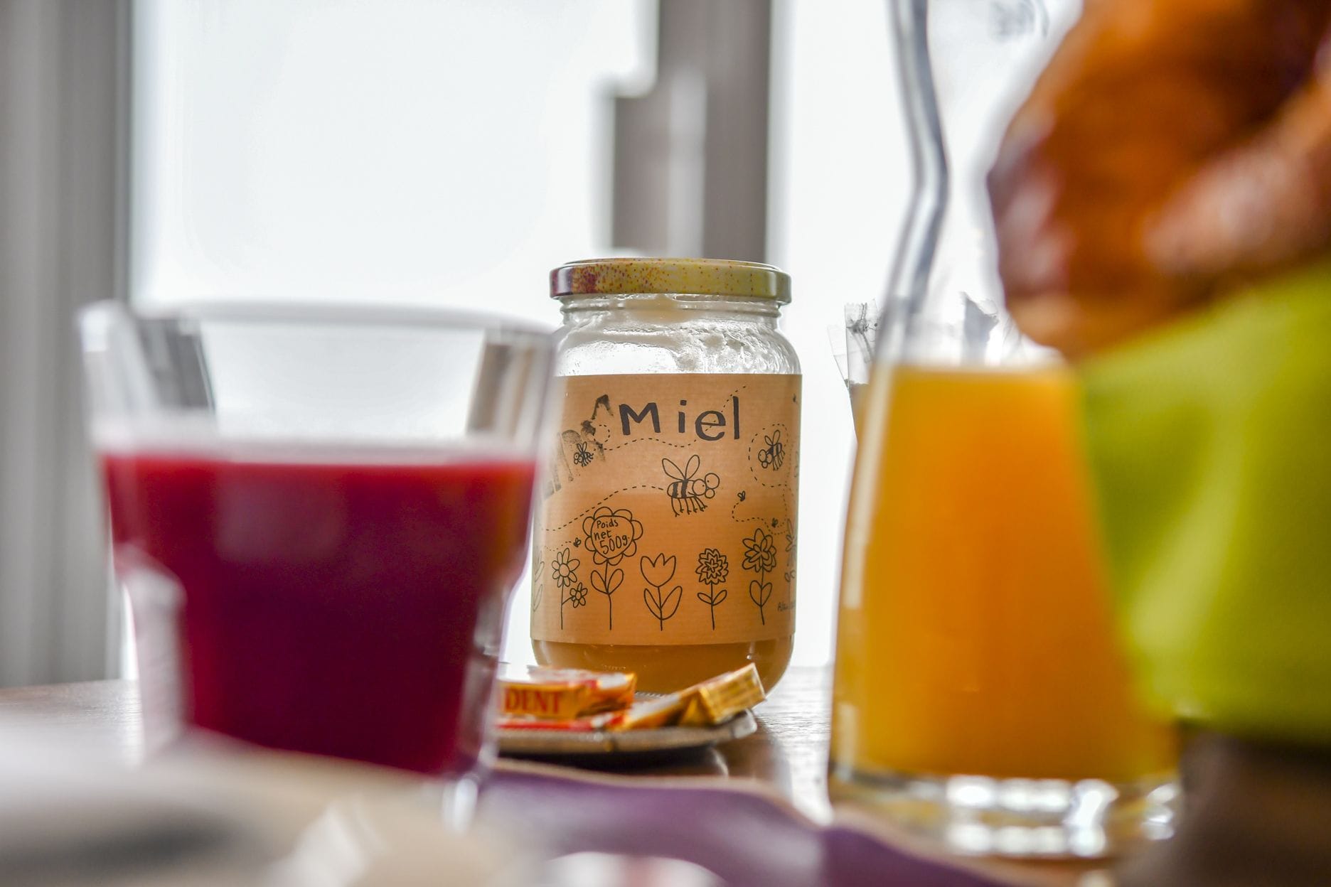 Un tarro de vidrio con una etiqueta que dice "Miel" y un vaso de jugo de naranja sobre una mesa.