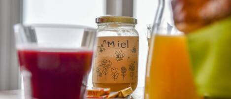 A glass jar with a label reading "Miel" and a glass of orange juice on a table.