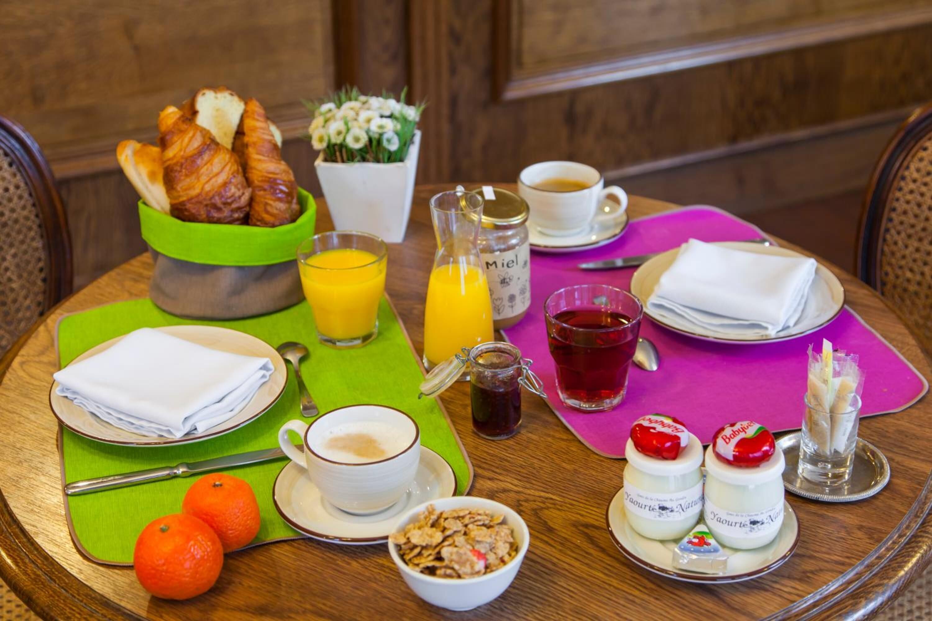 A breakfast table with croissants, orange juice, coffee, tea, and yogurt parfaits.