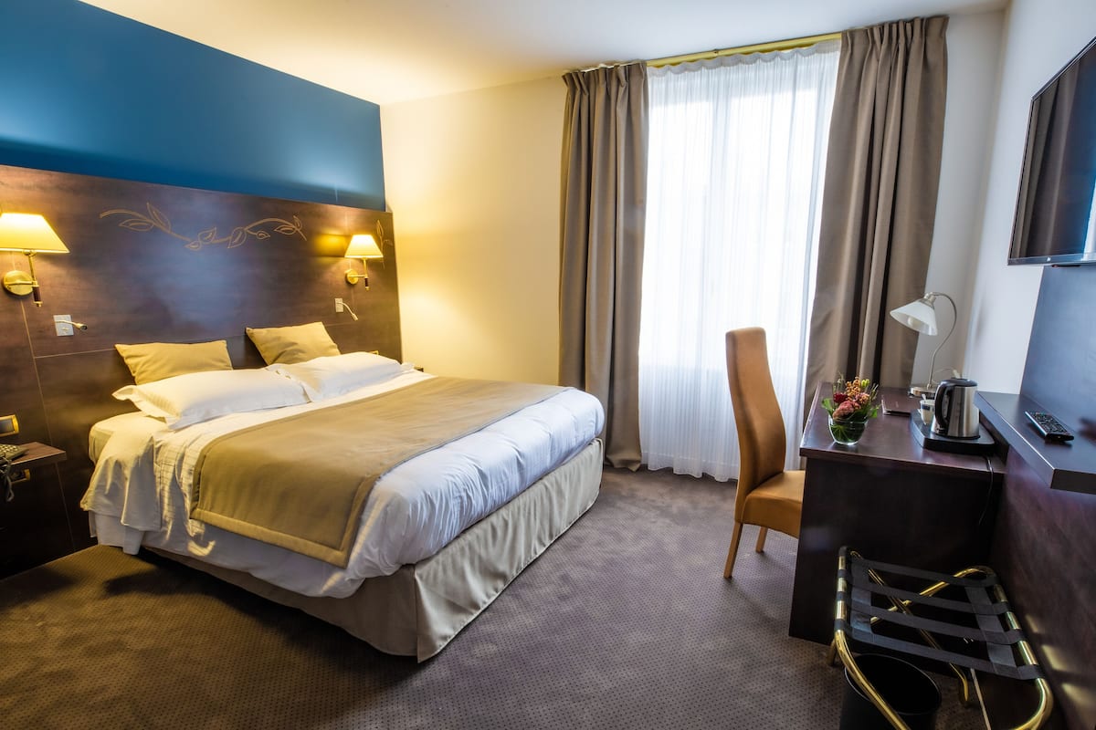 A hotel room with a bed, a desk, a chair, a TV, and a lamp.