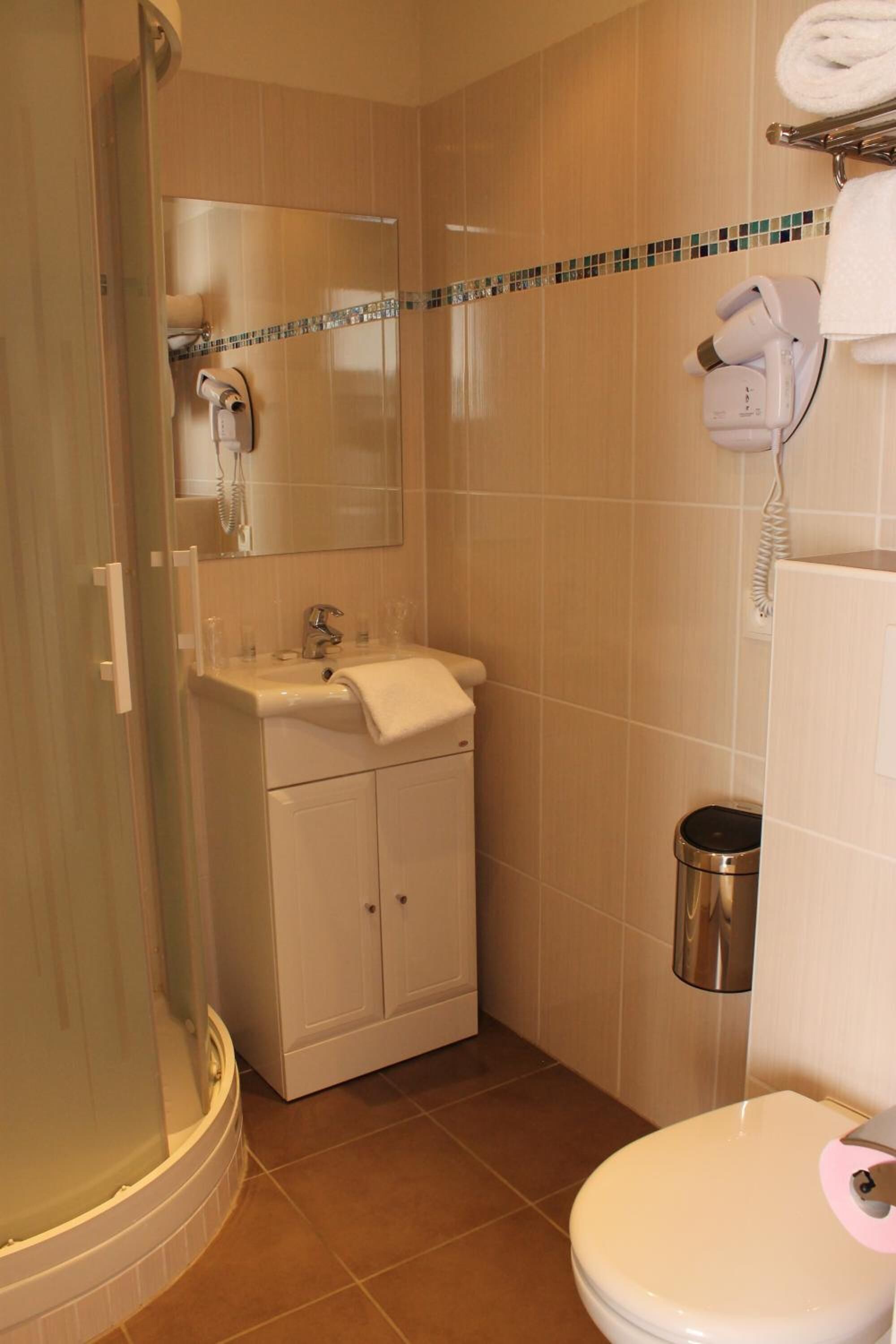 Un baño con ducha, lavamanos, inodoro y un secador de pelo en la pared.