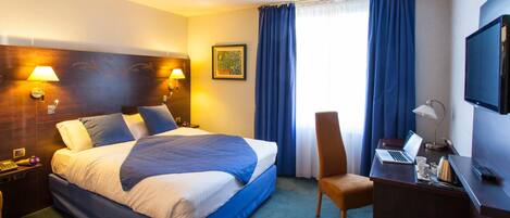 Una habitación de hotel con una cama grande, dos lámparas de noche, un escritorio con una computadora portátil, una silla y un televisor.