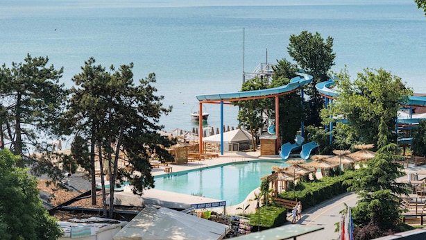 A pool area with a water slide, lounge chairs, and a view of the sea. - Palm Beach Hotel- All Inclusive (Golden Sands)