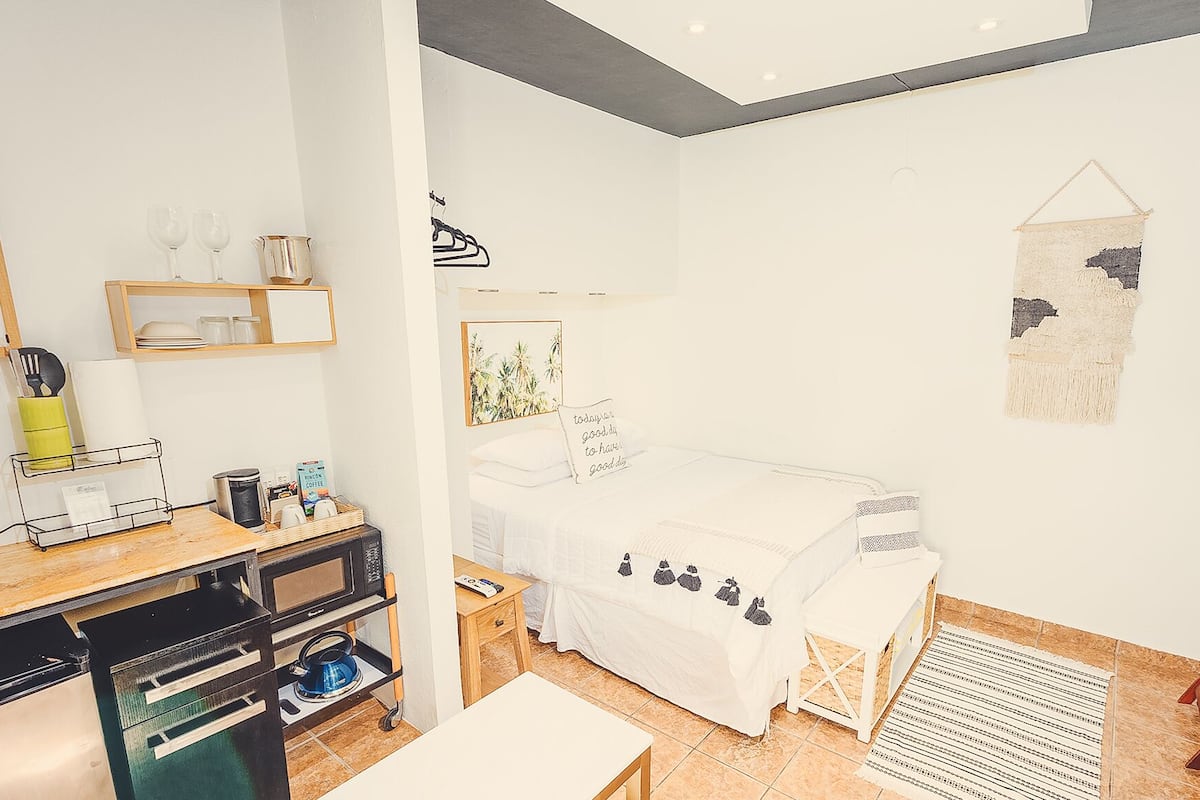 Quarto moderno com cama, mesa de cabeceira e pequena área de trabalho com cadeira.
