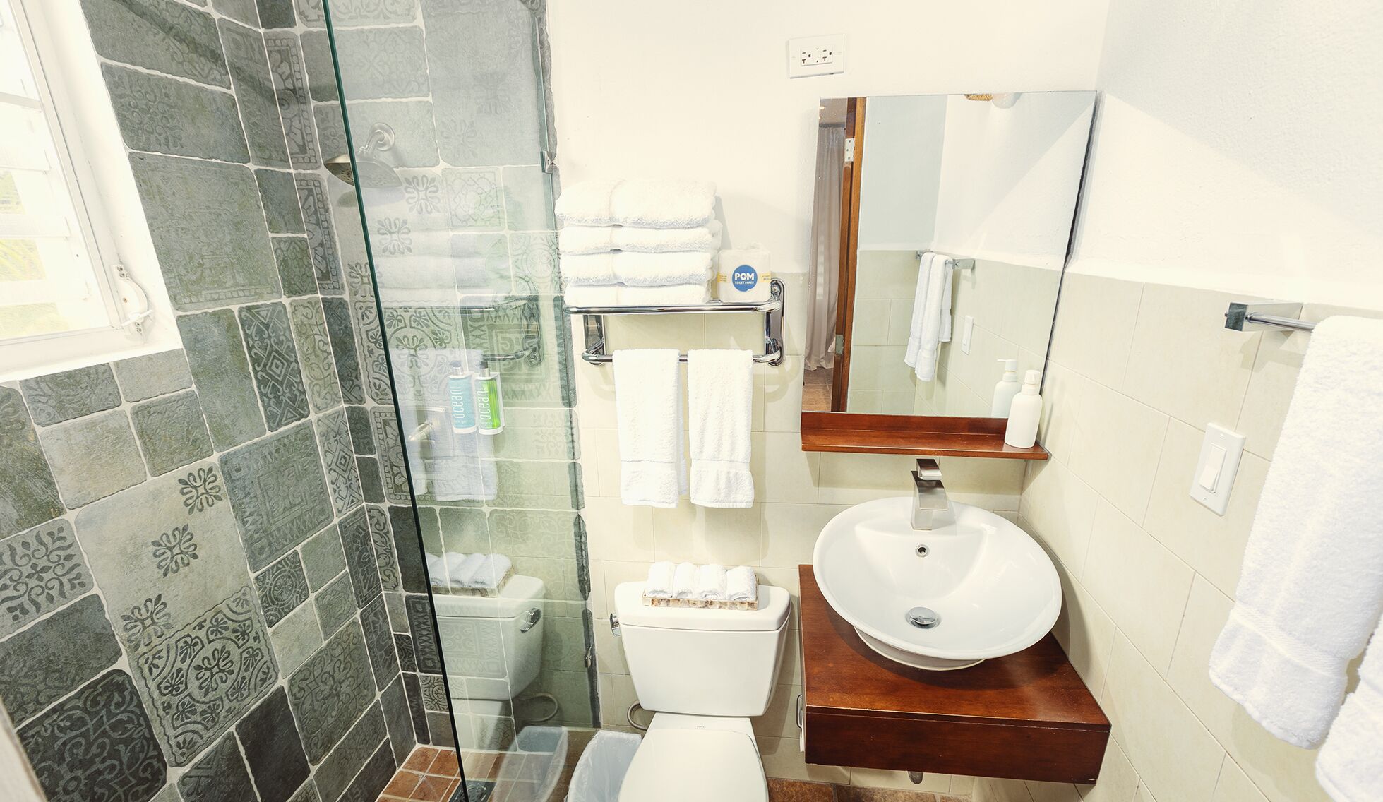 Un baño con cabina de ducha de vidrio, inodoro blanco, lavamanos con encimera de madera y espejo sobre el lavamanos.