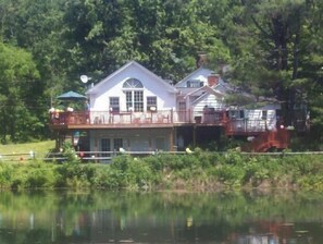 Un chalet au bord du lac, doté d’une grande terrasse et de nombreuses fenêtres, entouré d’une forêt dense.