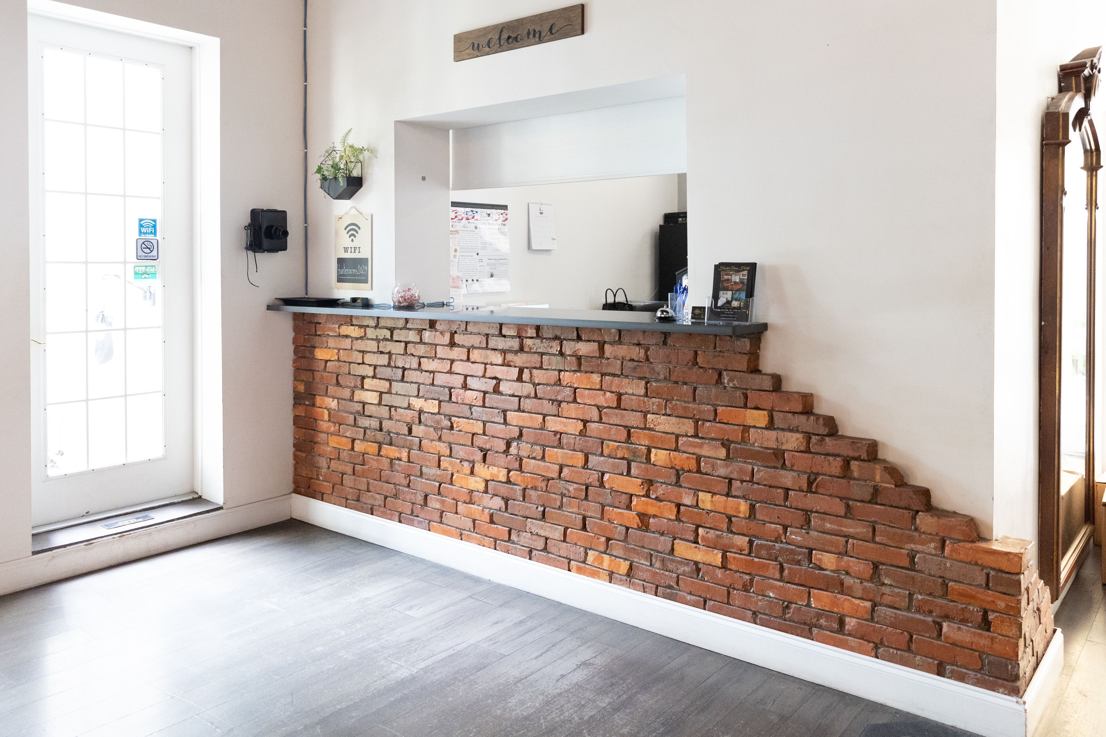 Un espace d’accueil avec un mur en briques, une porte blanche et une enseigne sur laquelle on peut lire « Bienvenue ».