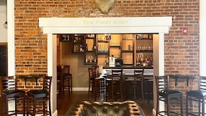 Een bar met een bakstenen muur, een opgehangen hertenkop en een leren fauteuil op de voorgrond.