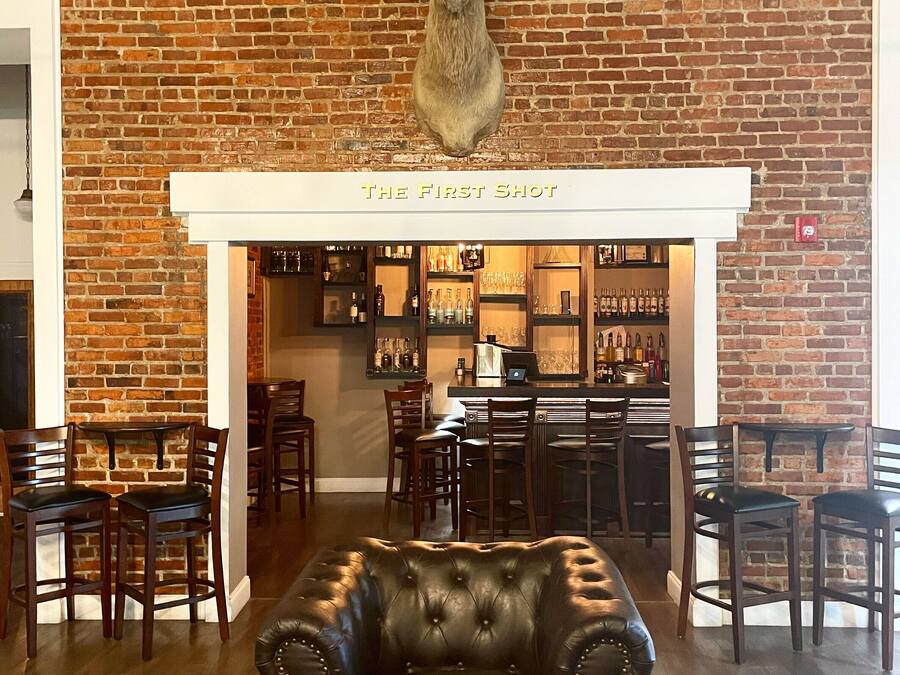 A bar area with a brick wall, a mounted deer head, and a leather chair in the foreground.