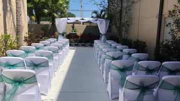 A pathway lined with white chairs with green sashes, leading to a white archway with a fountain.