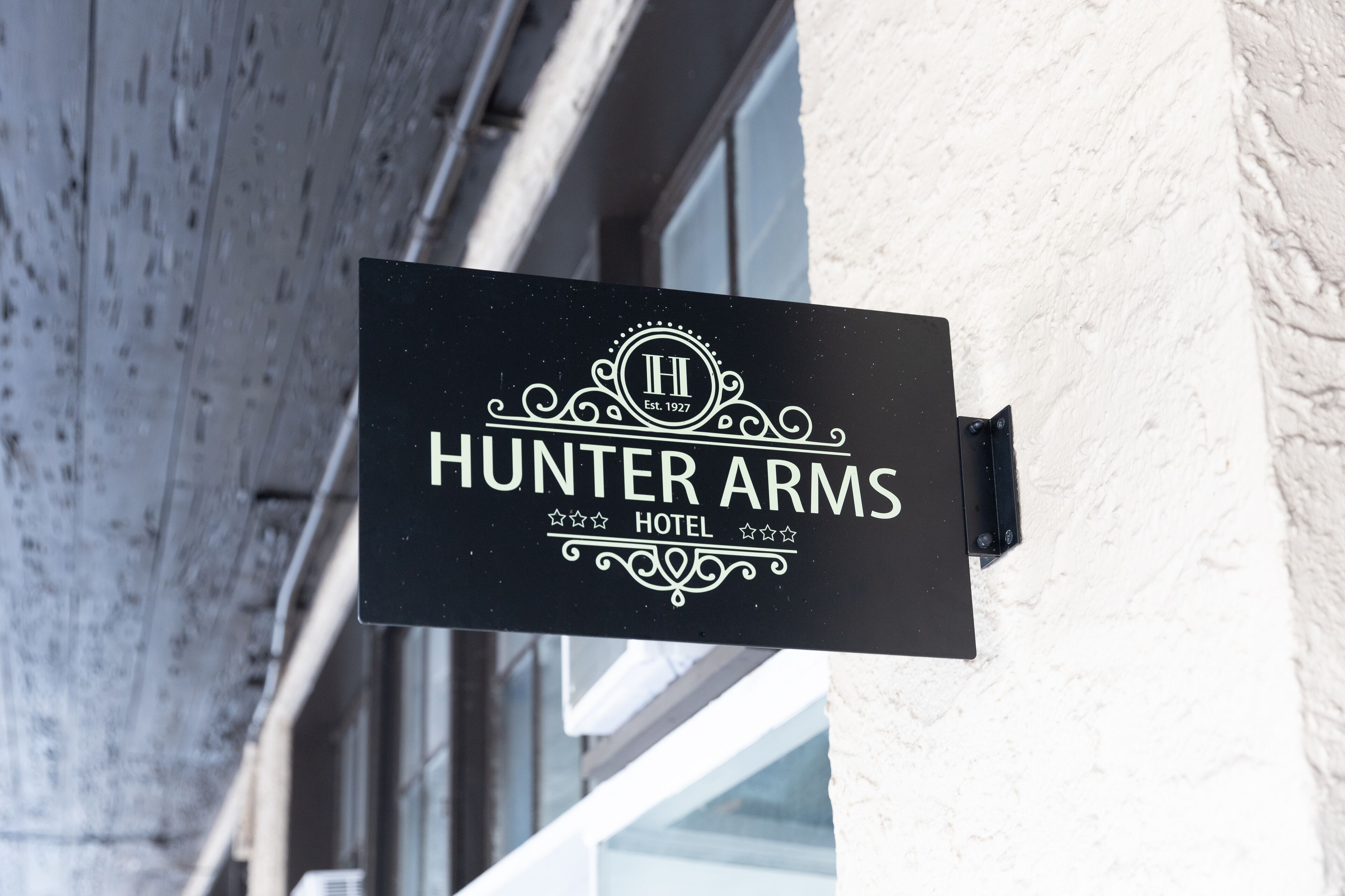 Une enseigne noire portant l’inscription « Hunter Arms Hotel » et un logo, fixée sur un bâtiment.