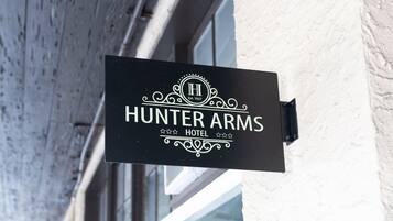 Une enseigne noire portant l’inscription « Hunter Arms Hotel » et un logo, fixée sur un bâtiment.