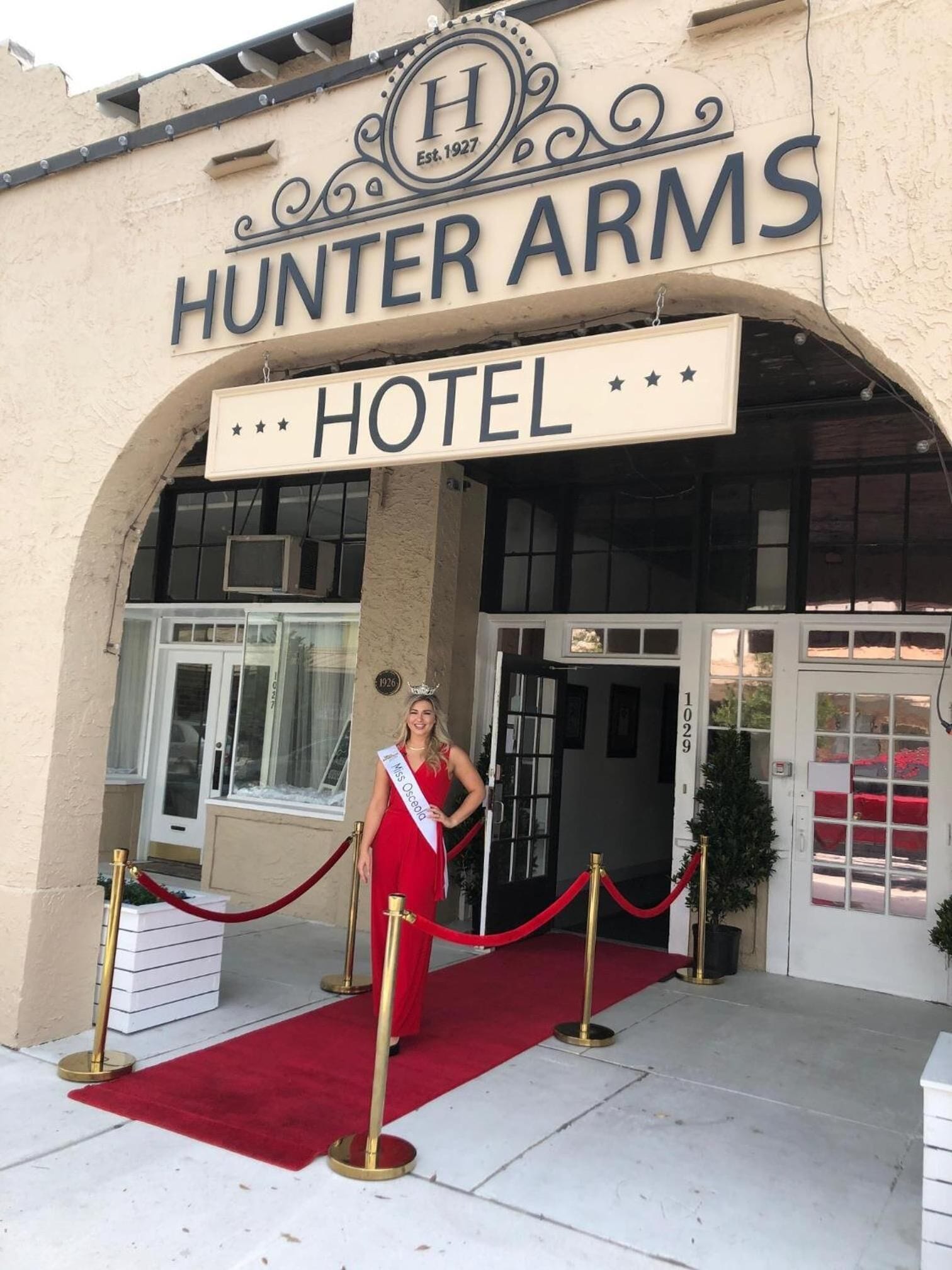 A hotel entrance with a sign reading "HUNTER ARMS HOTEL" and a red carpet leading to the door.