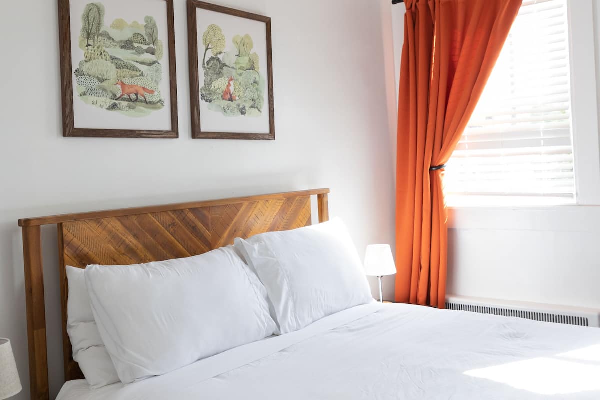 A neatly made bed with white linens, a wooden headboard, and two framed landscape paintings on the wall.