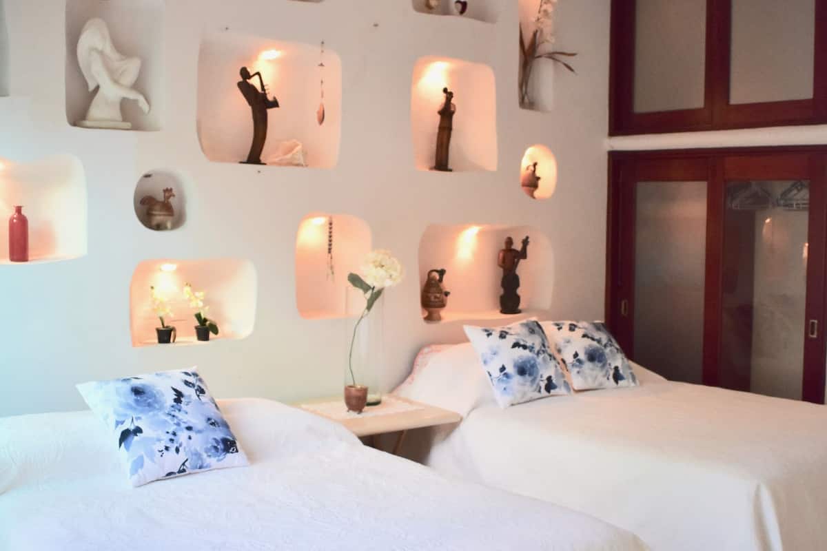 A hotel room with two beds, a ceiling fan, and decorative wall niches.