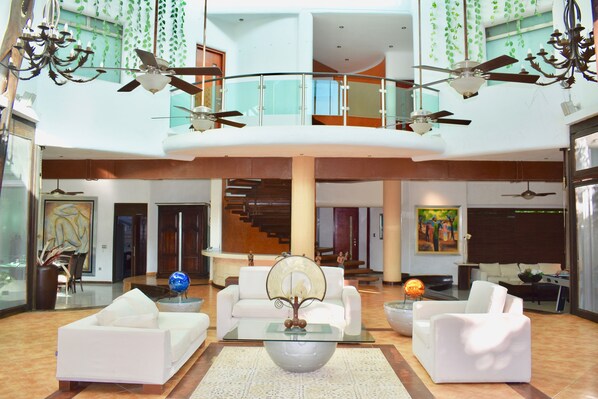 A spacious living area with a high ceiling, multiple ceiling fans, and a central glass coffee table. - Casa La Selva (Cancun)