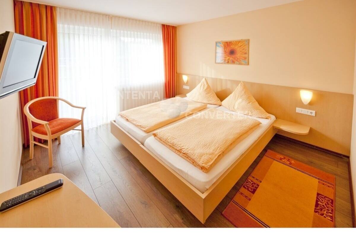 Een hotelkamer met een bed, een televisie, een stoel en een raam met gordijnen.