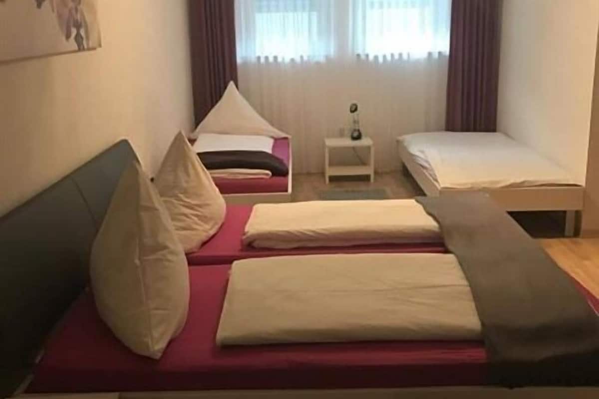 Een kamer met twee bedden, één met een rode matras en de ander met een witte matras. Er staat een klein nachtkastje met een lamp erop.