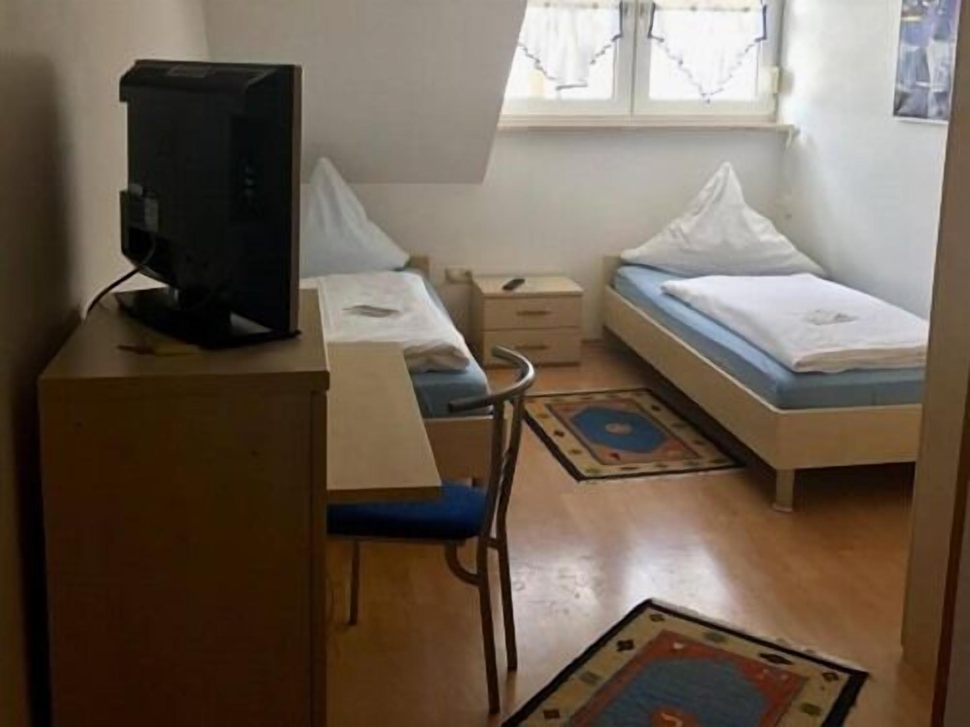 Una habitación pequeña y poco amueblada con escritorio, silla, cama y ventana.