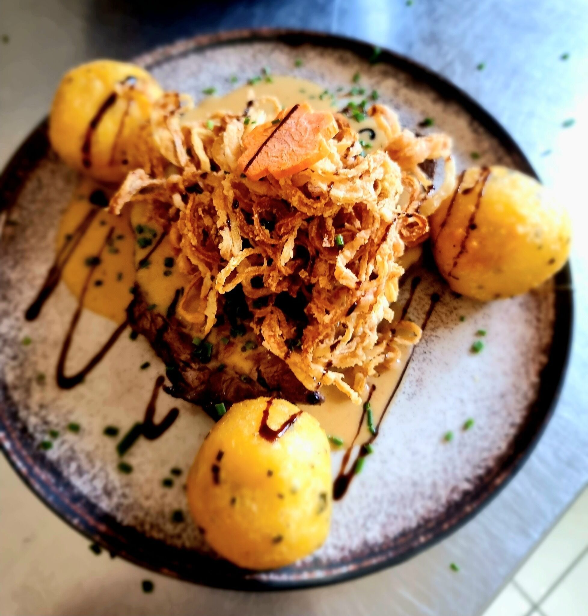 Ein Teller Essen mit einem Steak, gebratenen Zwiebeln und Kartoffeln.