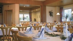 Un espace repas avec des tables dressées pour le repas, des chaises en bois et une croix accrochée au mur.