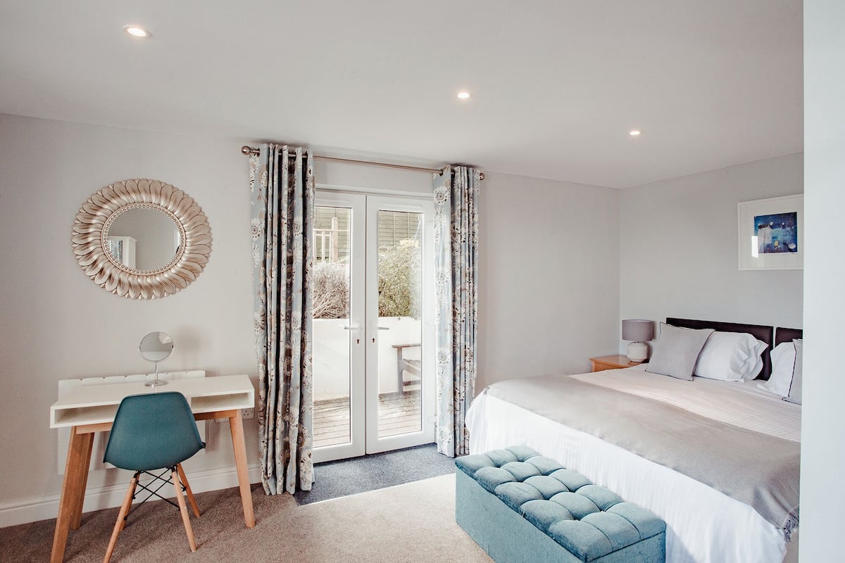 A bedroom with a bed, a desk, a chair, a round mirror, and a window with curtains.