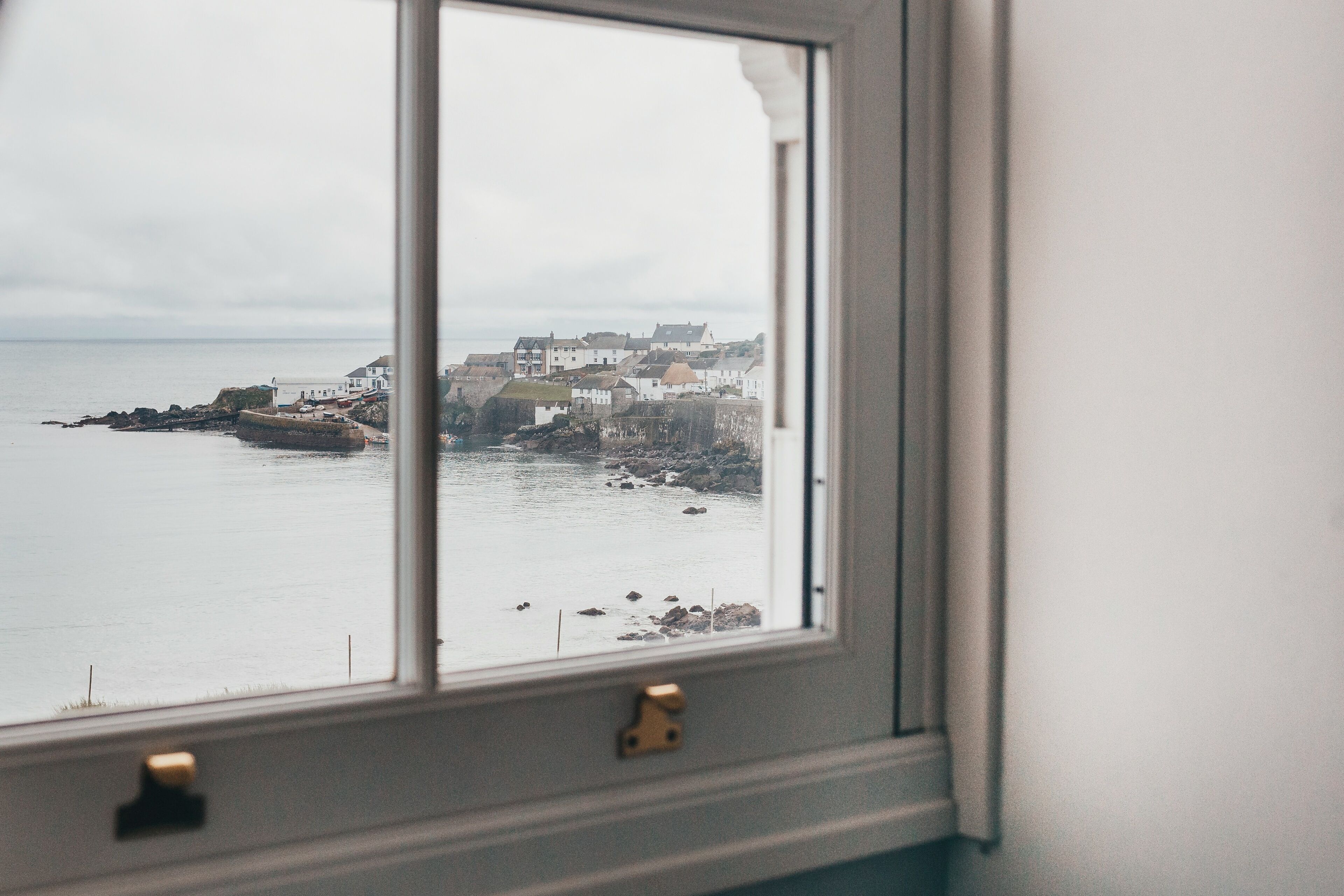 A coastal town view through a window with a white frame and a brass handle.