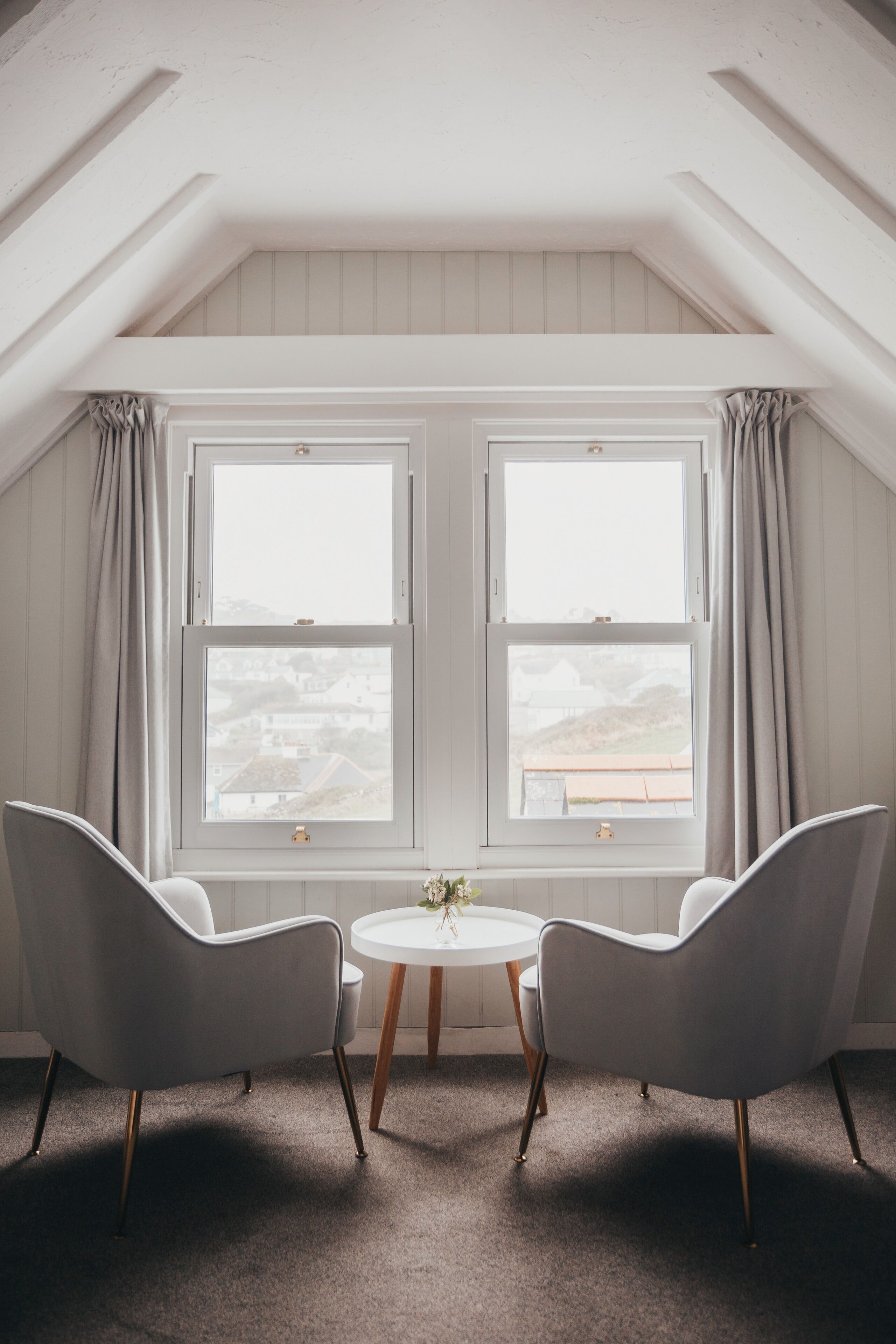 A room with two white chairs, a small round table, and a view through large windows.