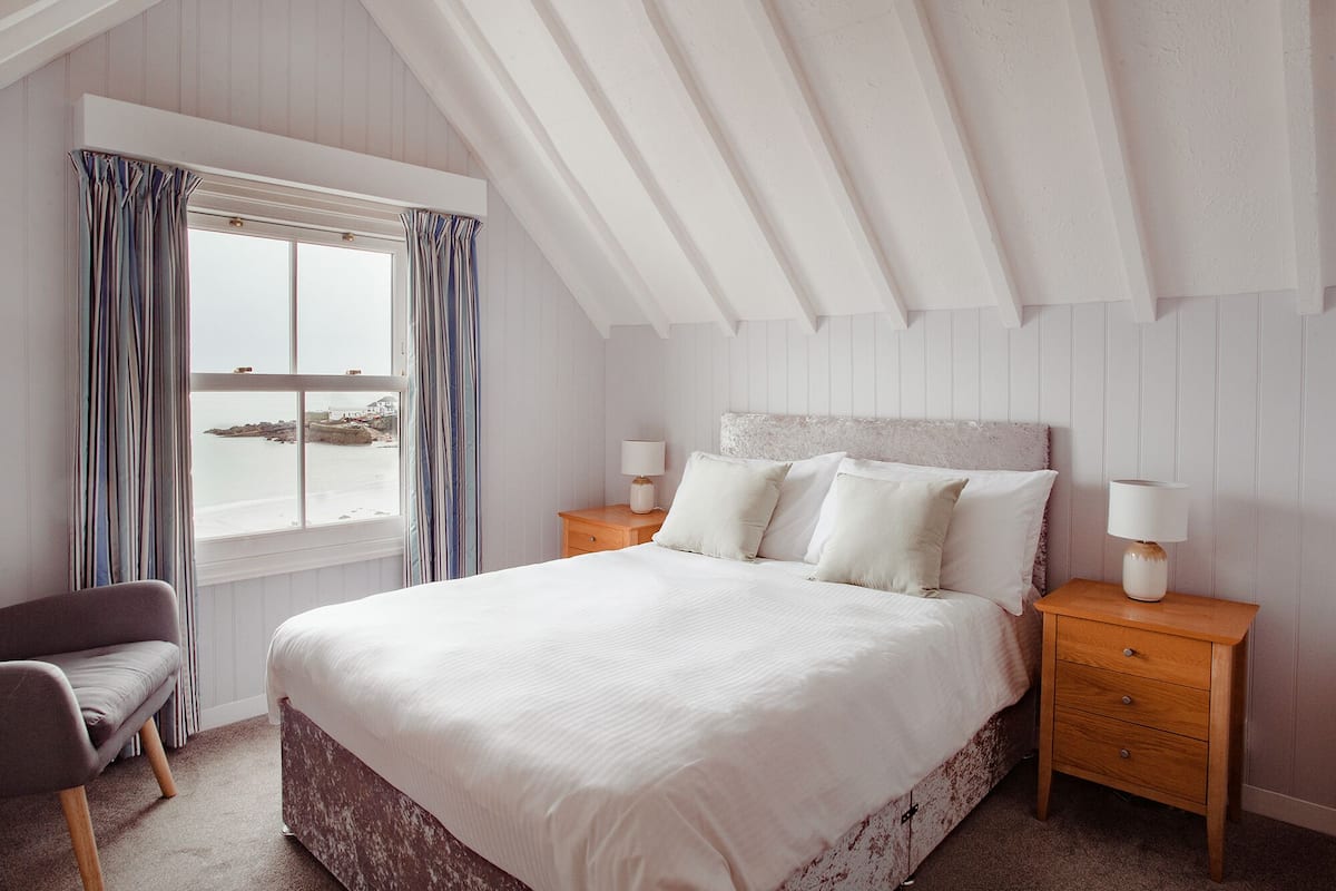 A bedroom with a large bed, two bedside tables with lamps, a chair, and a window with curtains.