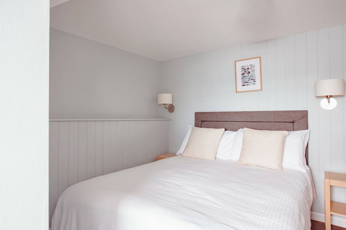 A neatly made bed with white bedding, a wooden headboard, and two bedside lamps.