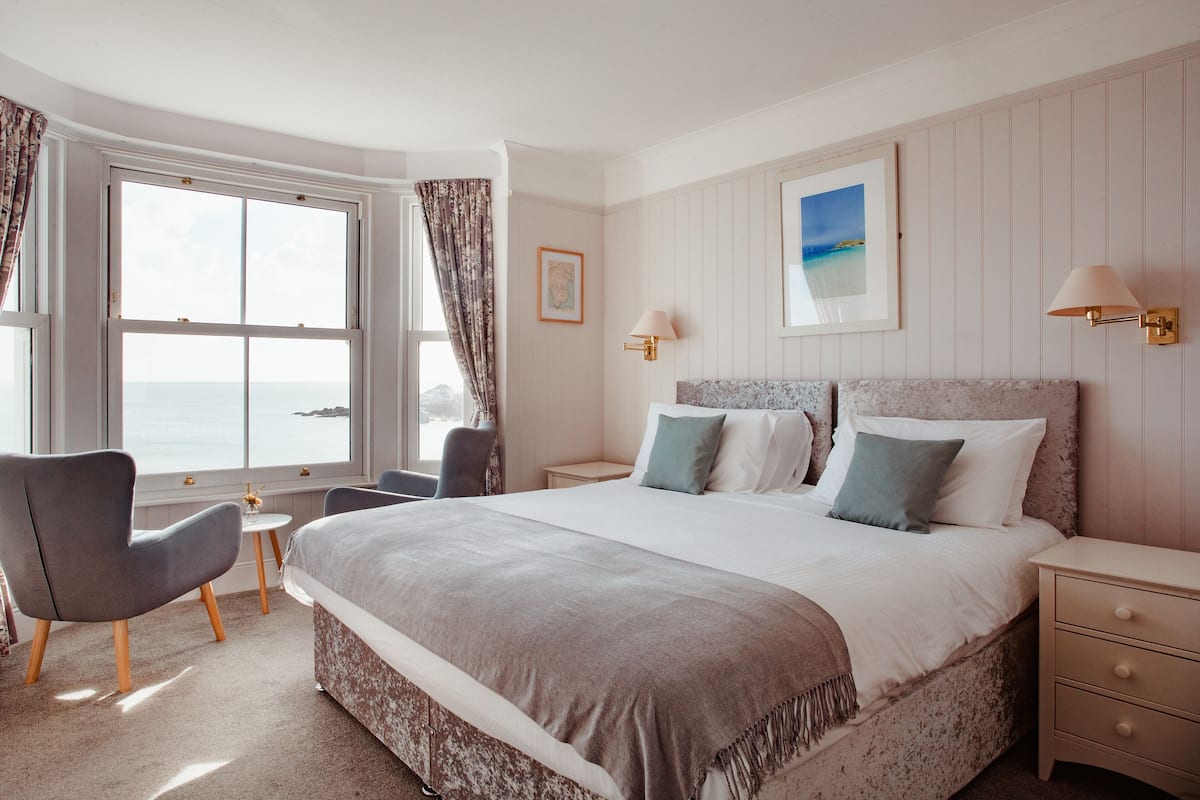A hotel room with a large bed, a small desk, a chair, and a view of the sea.