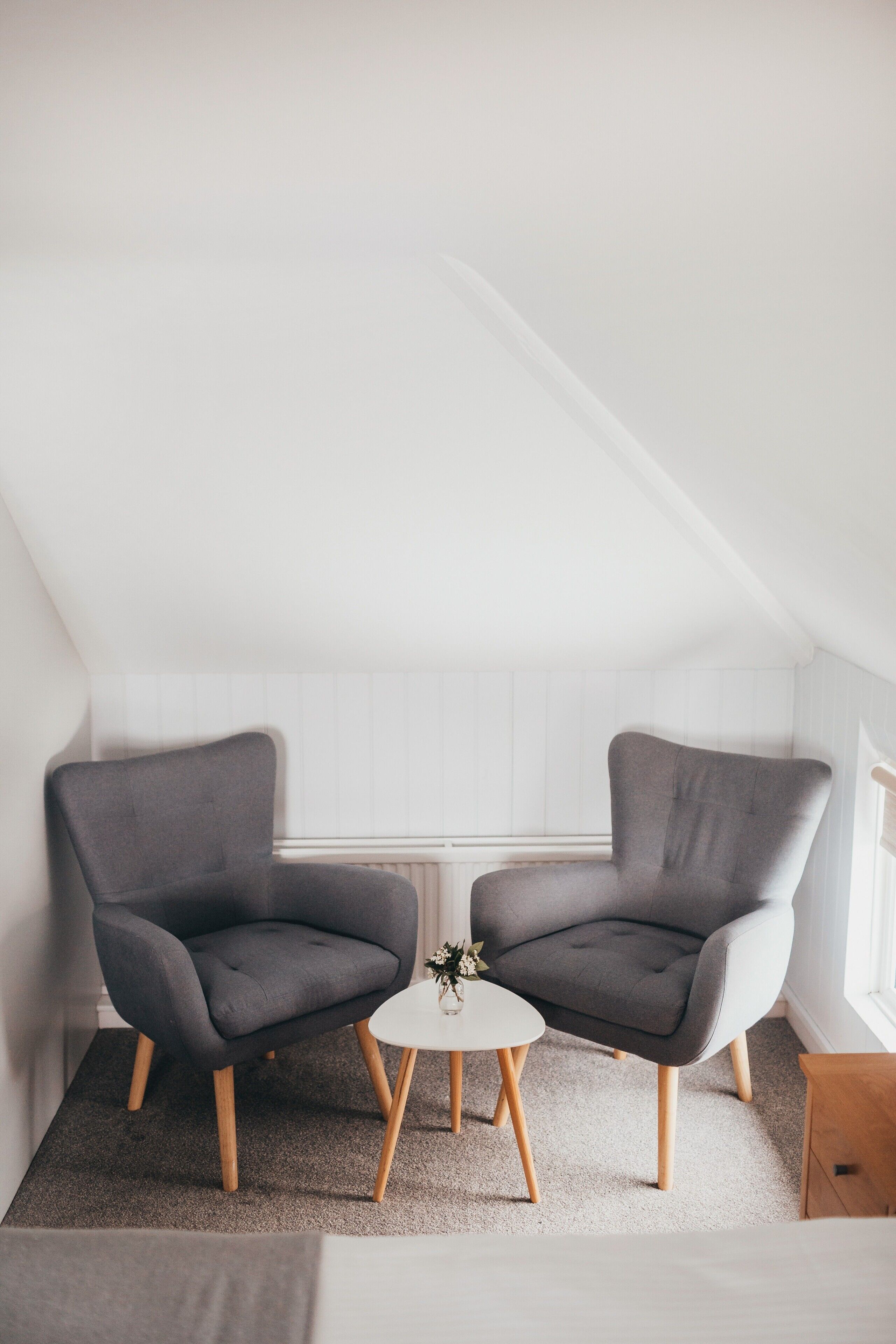 A small, modern room with two grey armchairs, a small white table, and a wooden nightstand.