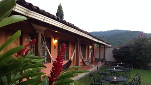 A building with a tiled roof, a covered porch, and outdoor seating with tables and chairs. - La Casa de Cafe (Copan Ruinas)