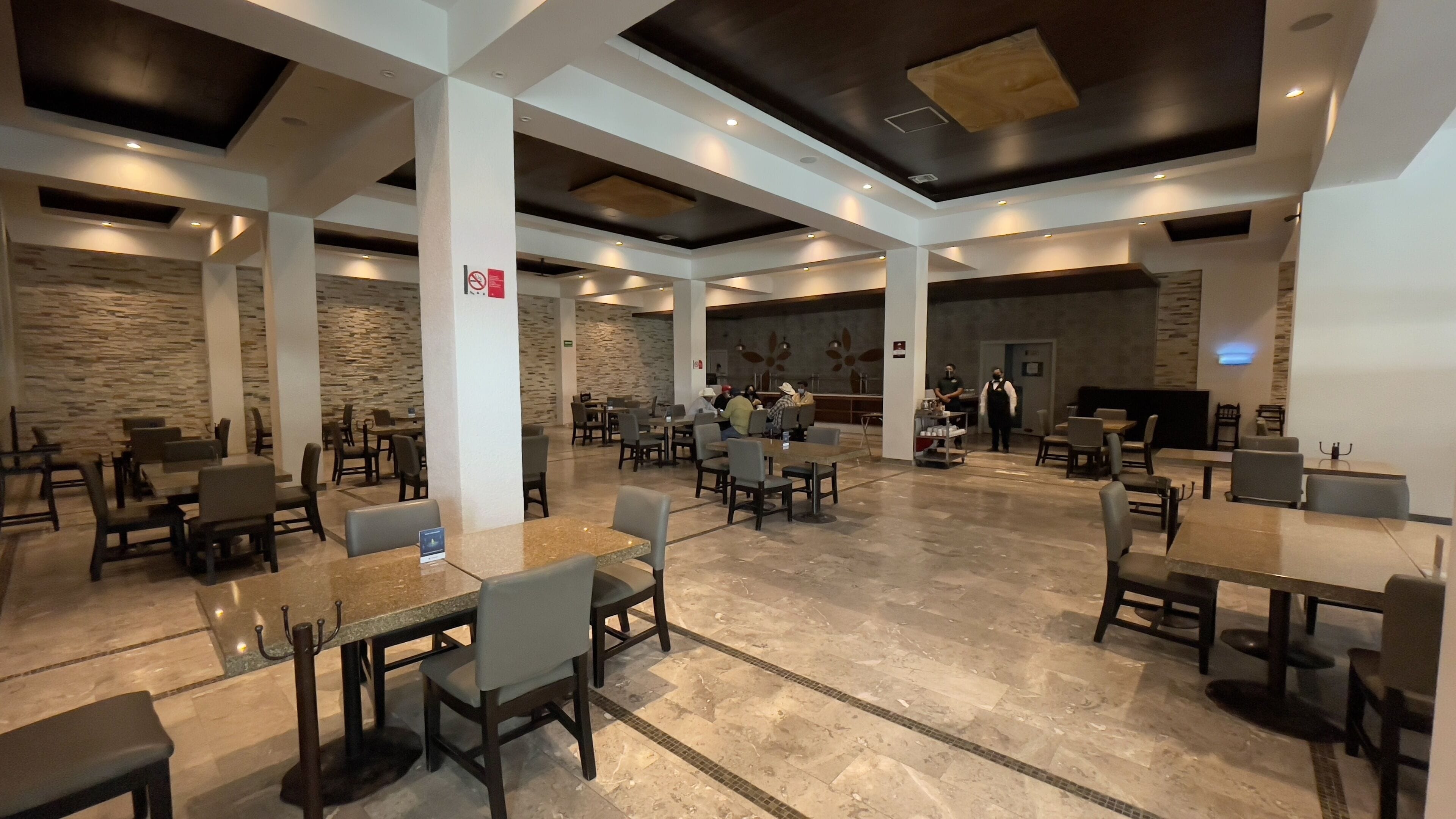 A spacious indoor dining area with multiple tables and chairs, stone walls, and a modern ceiling design.