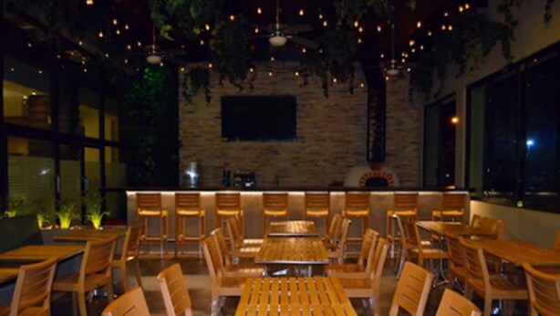 Un restaurante con mesas y sillas de madera, una pared de piedra y luces colgantes.