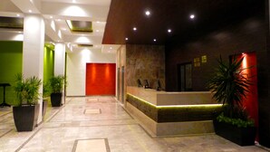Un lobby moderno con una recepción, plantas en macetas y una pared verde y roja.