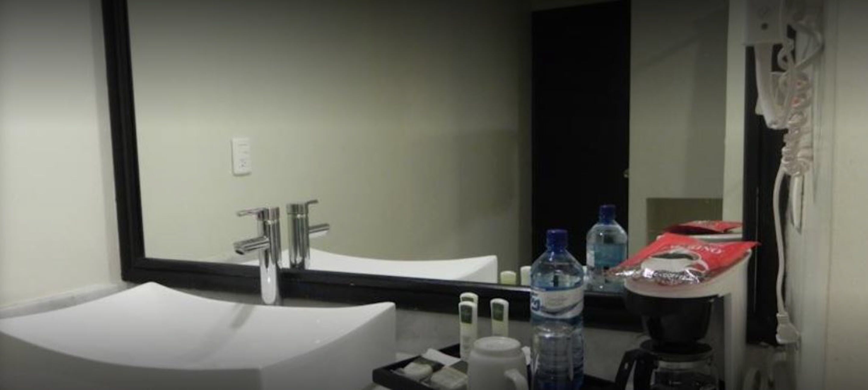 Une salle de bain d’hôtel avec un lavabo blanc, un miroir, un robinet, une machine à café et des articles de toilette.