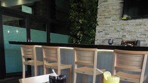 Una mesa de comedor con diversos platos, incluyendo pizza, costillas y una ensalada. Hay sillas alrededor de la mesa y un televisor montado en la pared al fondo.