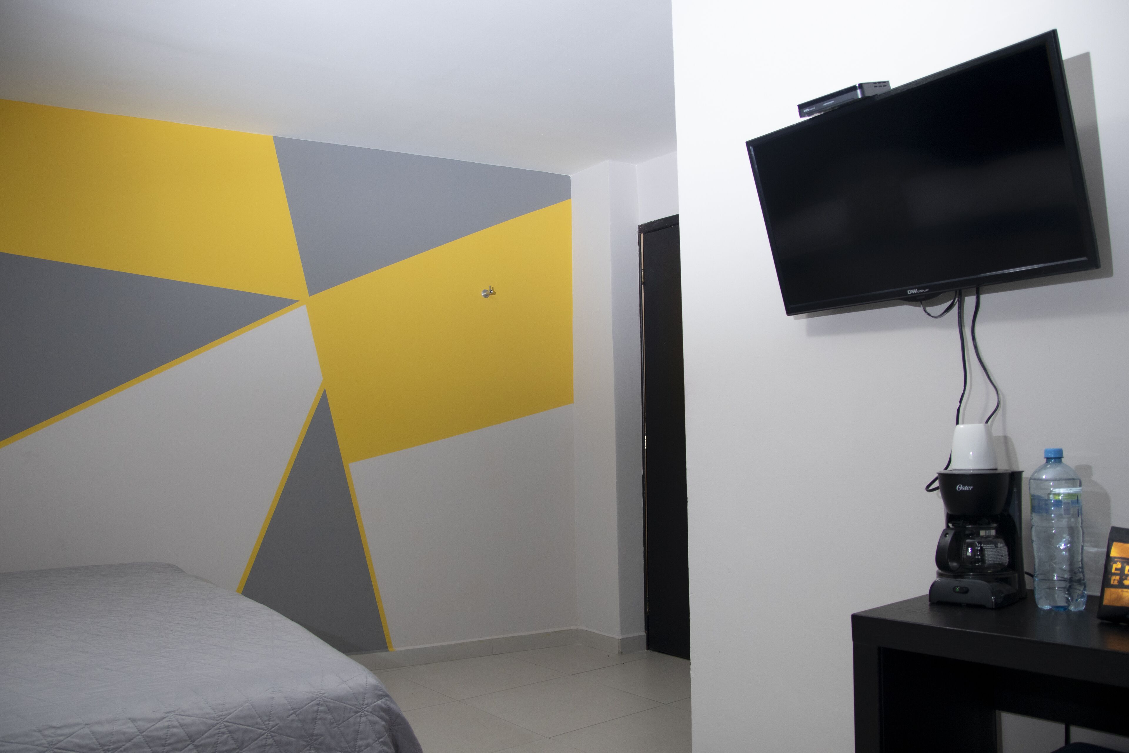 Una habitación de hotel con cama, televisor montado en la pared, cafetera y una botella de agua sobre una mesita.