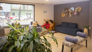Un hall de hotel con un sofá, sillones, una mesa de centro y una planta grande.