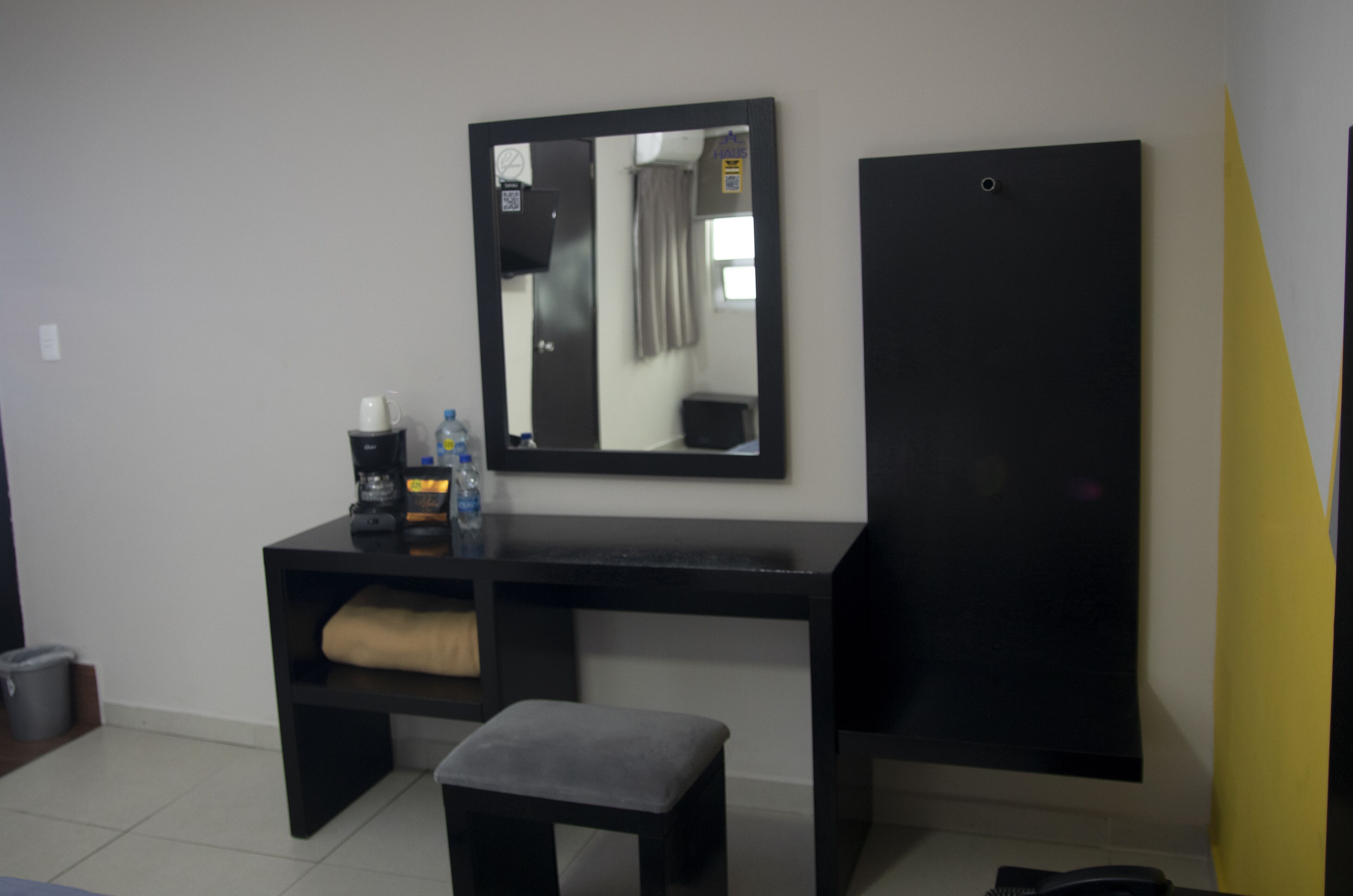 Habitació petita i moderna amb un escriptori negre, un mirall, una banca i un armari negre.